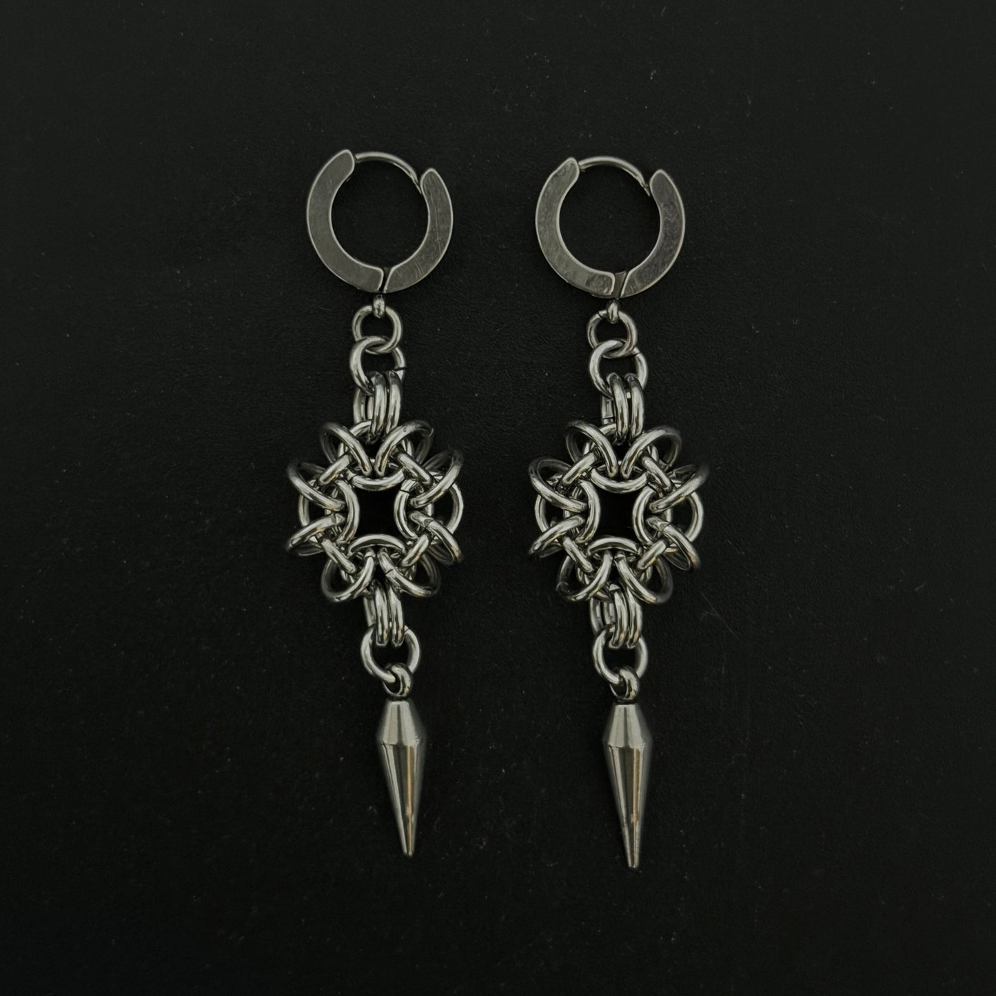 Pair of silver hoop earrings with star-shaped pendants and spike details on a black background