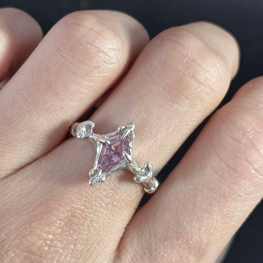 Silver ring with a pink gemstone on a finger
