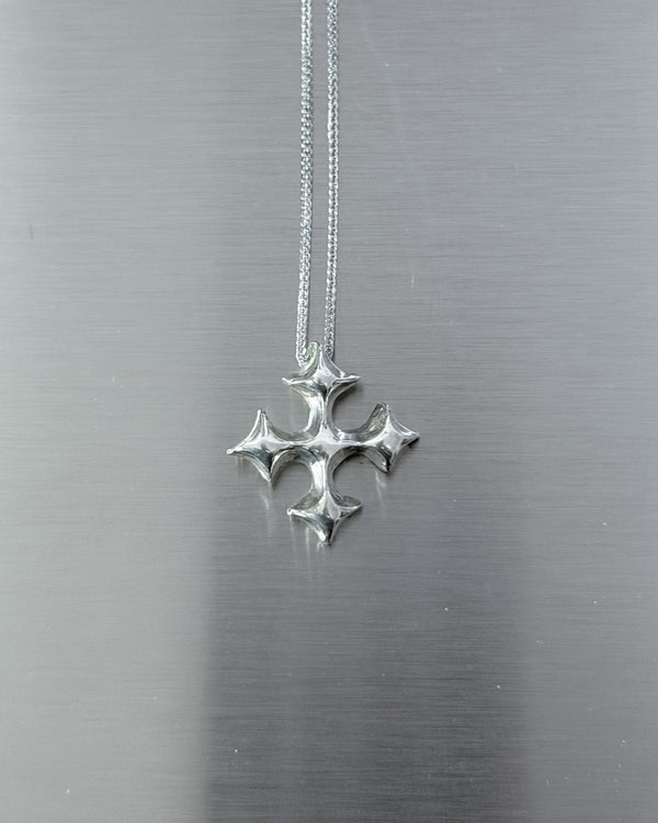 A silver cross pendant hanging from a delicate silver chain against a brushed metal background.