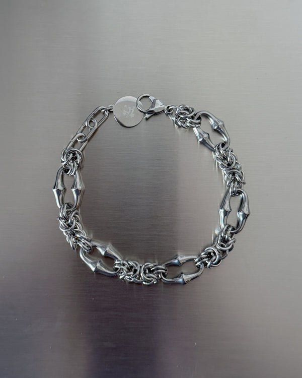 A silver-toned chain bracelet with alternating elongated oval links and smaller twisted chain sections, displayed on a brushed metallic surface.