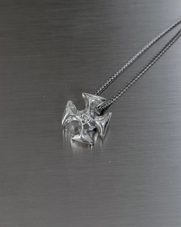 A silver necklace with a detailed cross pendant resting on a brushed metal surface.