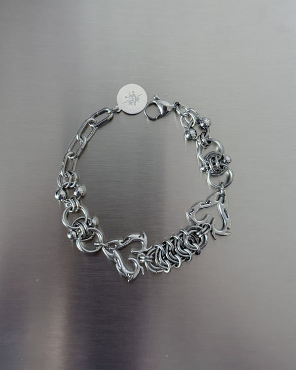 A silver-toned chain bracelet with a lobster clasp and a round engraved tag, photographed on a brushed metal surface.