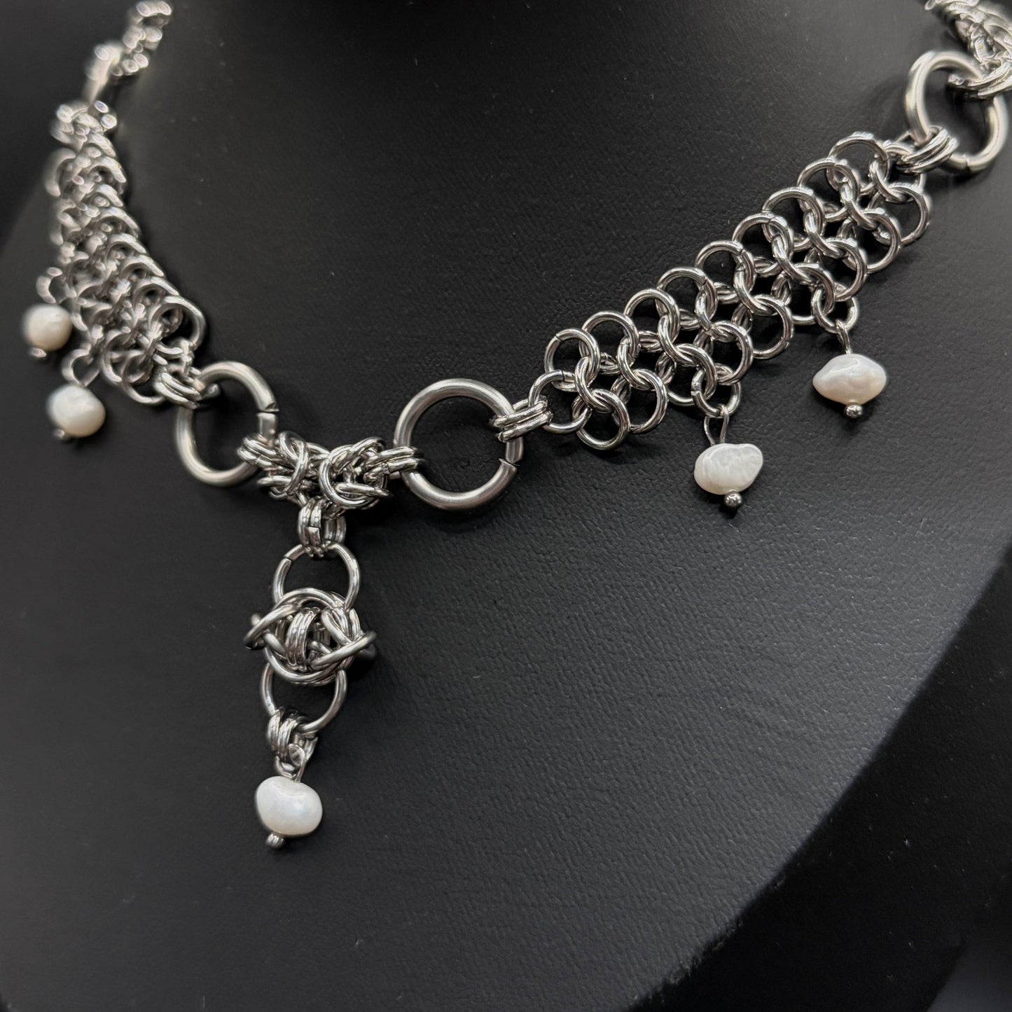 Silver chainmail necklace with pearl beads on a black stand