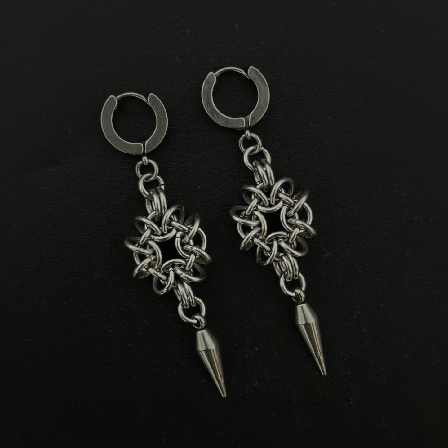 Pair of silver hoop earrings with chain and spike designs on a black background