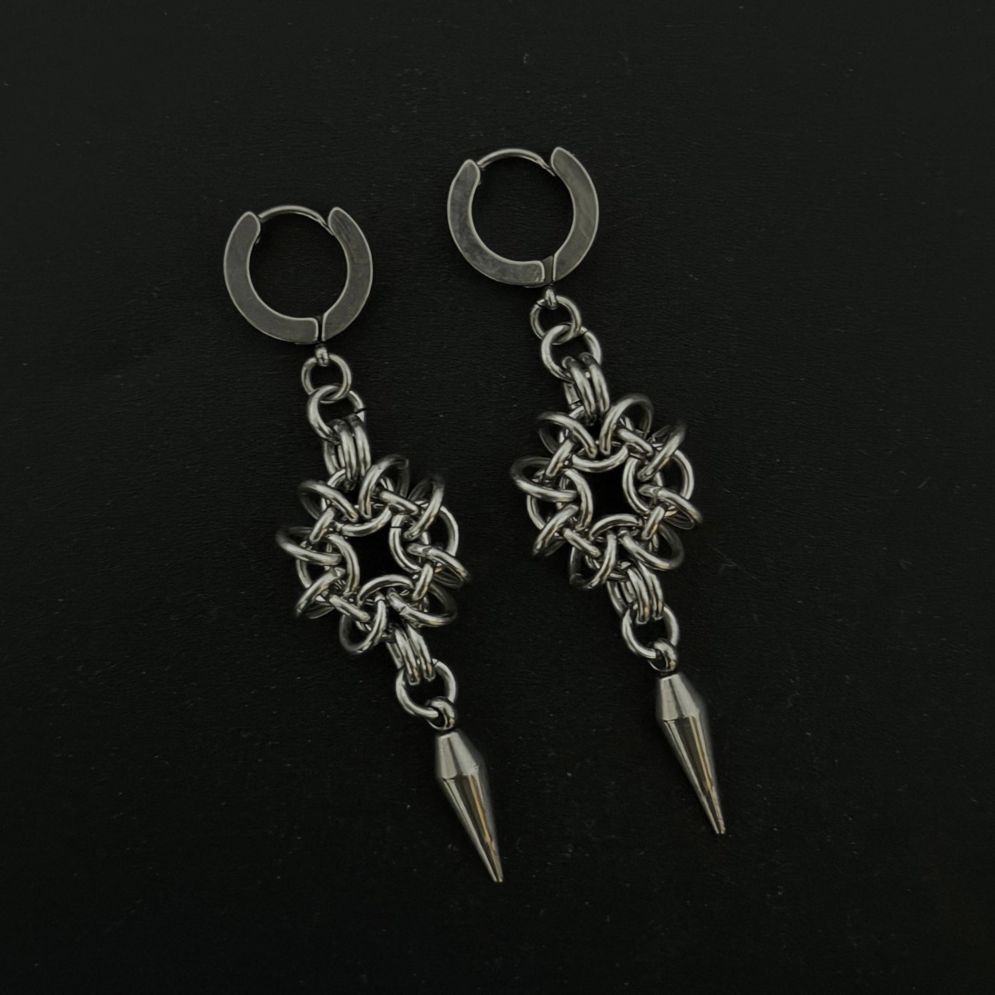 Pair of silver hoop earrings with chain and spike designs on a black background