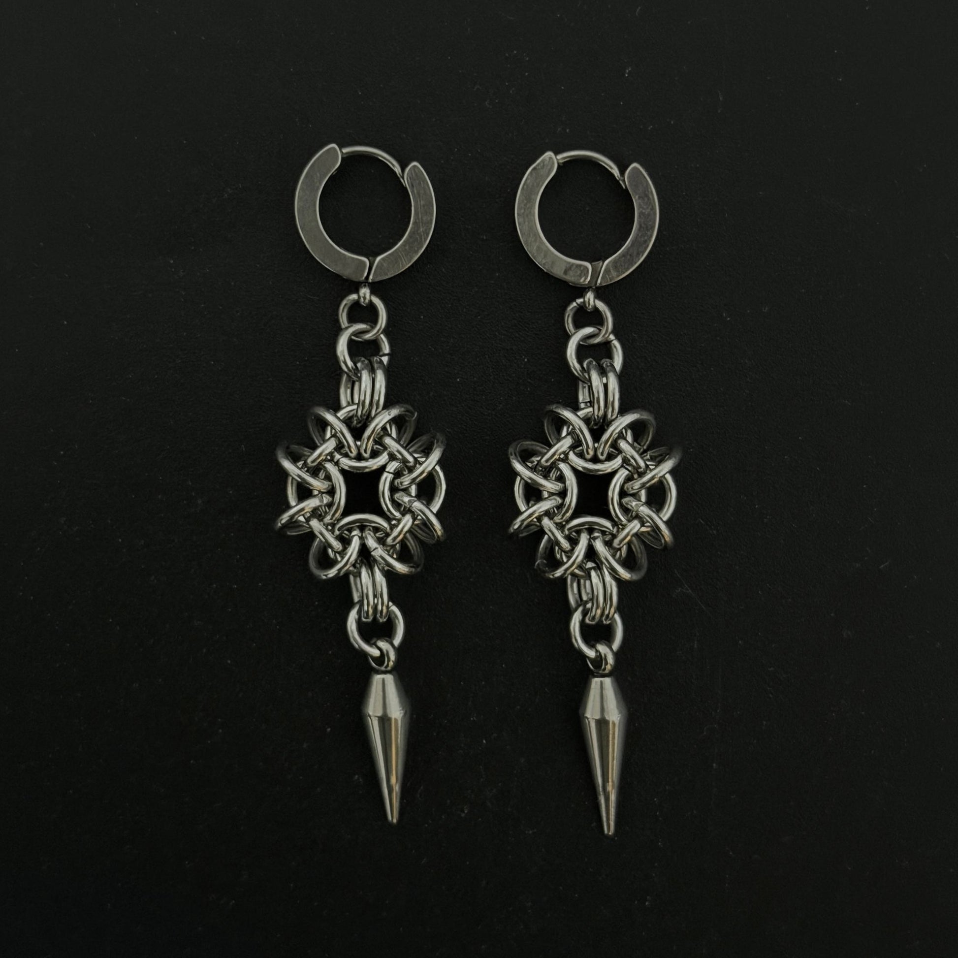 Pair of silver hoop earrings with star-shaped pendants and spike details on a black background