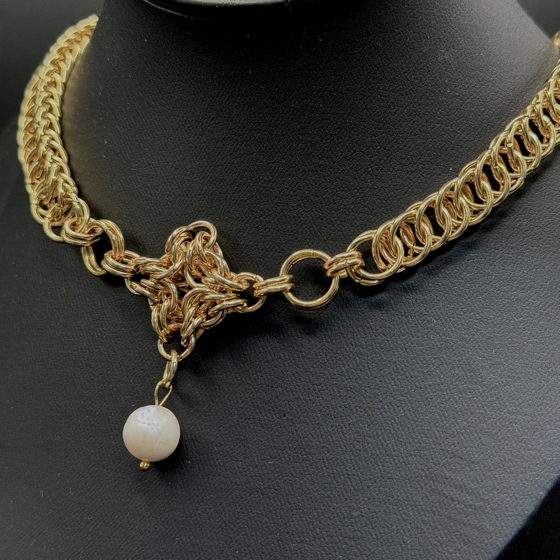 Gold chain necklace with a pearl pendant on a black mannequin head.