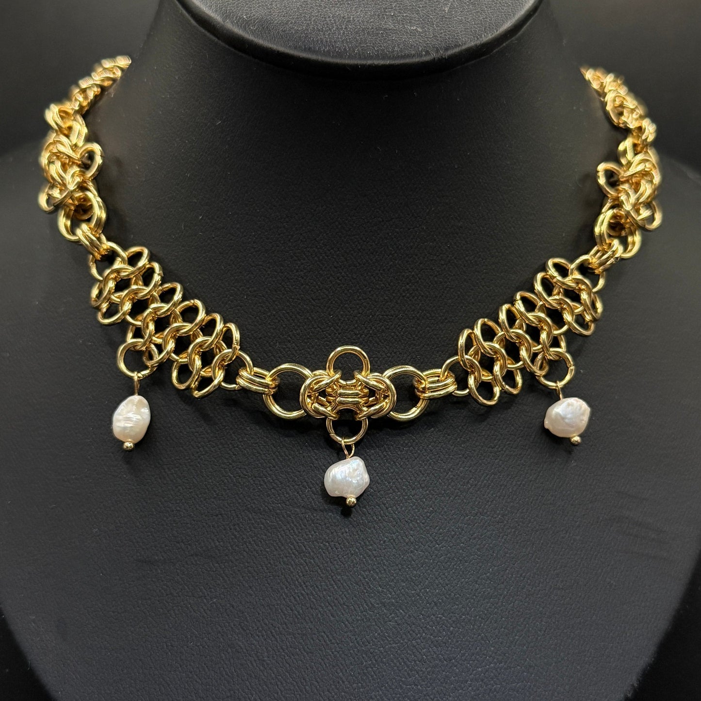 Gold chain necklace with pearl pendants on a black stand