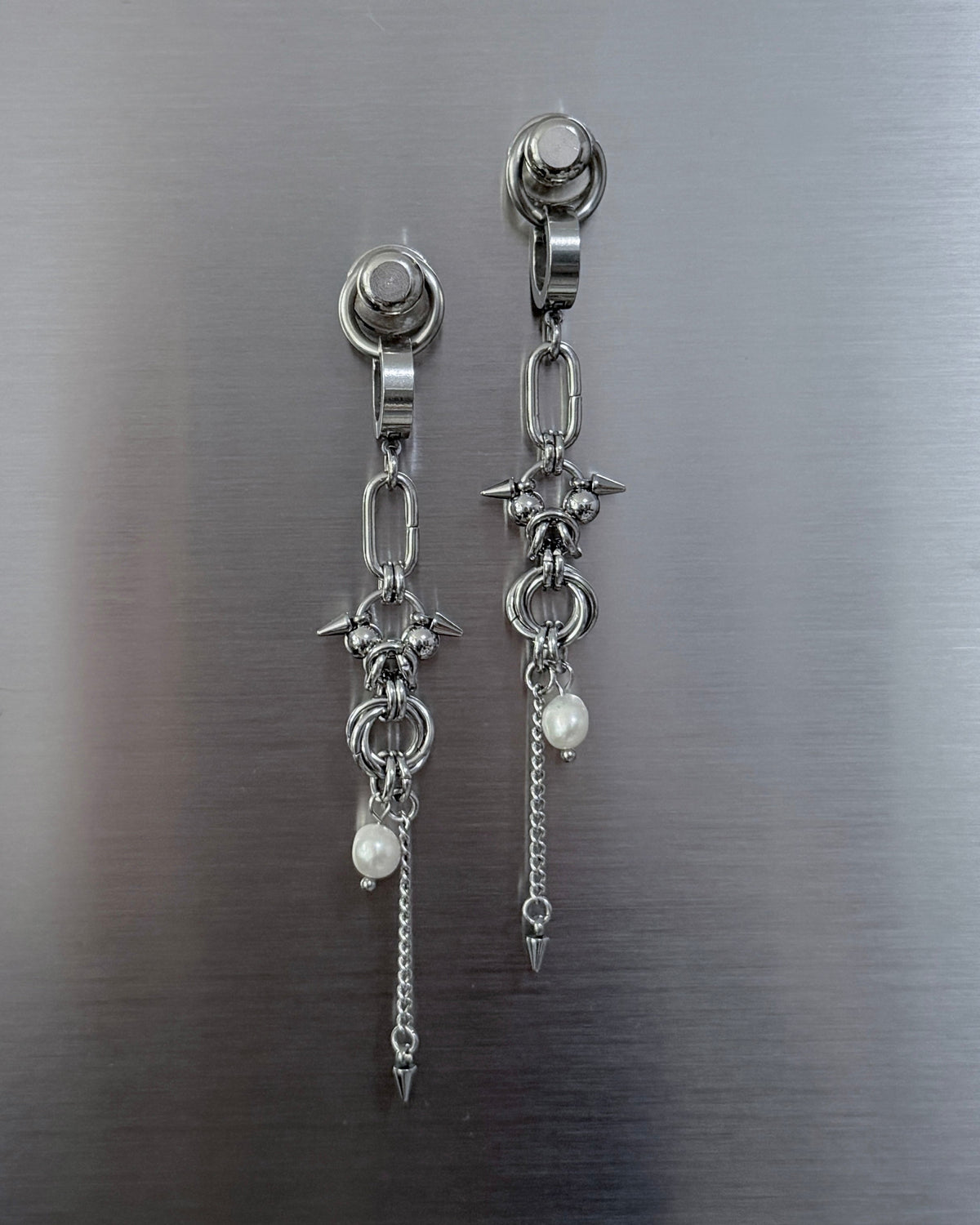 A pair of silver-toned dangle earrings with star and chain details, displayed on a brushed metal surface.